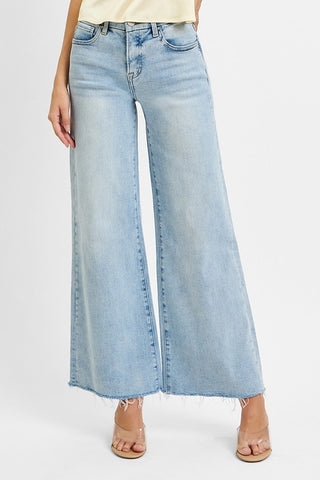 A woman wearing light wash wide leg jeans with a raw hem in a mid rise.