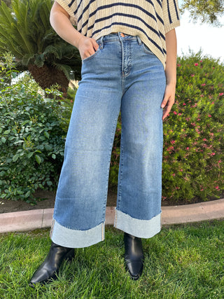 A woman wearing high-waisted cuffed wide-leg jeans in a medium wash and black boots.