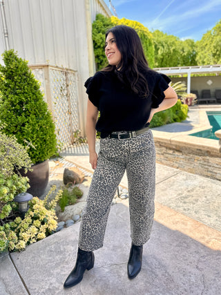 A woman wearing high waisted leopard print barrel leg pants with a light colored top and cowgirl boots.