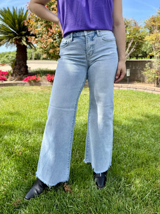A woman wearing light wash wide leg jeans with a raw hem in a mid rise.