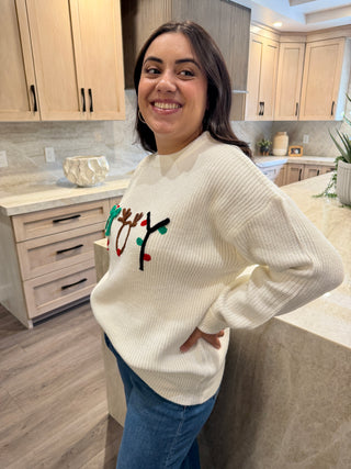 Woman wearing a white sweater with a colorful design in a kitchen