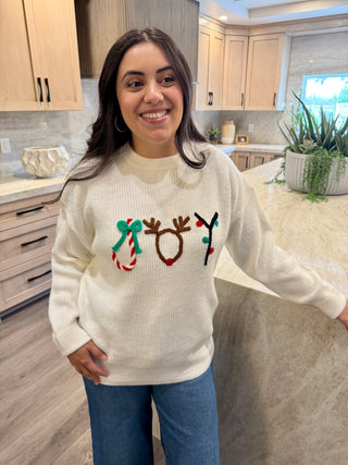 Woman wearing a cream sweater with Christmas-themed designs in a kitchen.