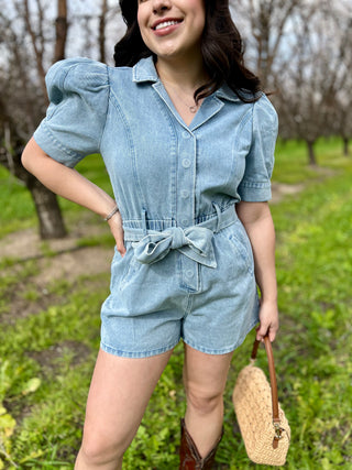 A woman wearing a blue denim romper with puffy sleeves and a matching belt.