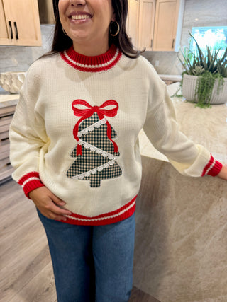 Person wearing a white sweater with a Christmas tree design in a kitchen.
