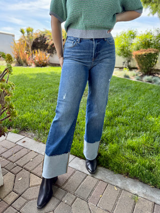 A woman wearing high waisted dark blue wide leg jeans with a big cuff paired with boots and a sweater.