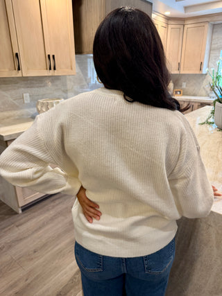 Person wearing a white sweater and blue jeans in a kitchen.
