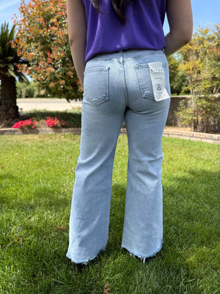 A woman wearing light wash wide leg jeans with a raw hem in a mid rise.