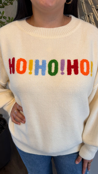 Cream-colored sweater with colorful 'HO! HO! HO!' text worn by a person.