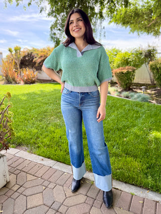 A woman wearing high waisted dark blue wide leg jeans with a big cuff paired with boots and a sweater.