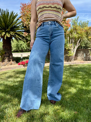 A woman wearing high waisted jeans that are a medium wash with a raw hem and are a wide leg style.