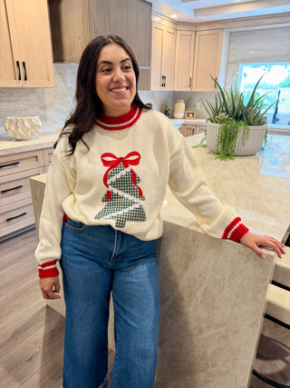 Woman wearing a festive sweater with a Christmas tree design in a kitchen.