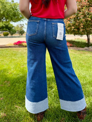 A woman wearing high rise wide leg jeans with a big cuff on the bottom in a dark wash.