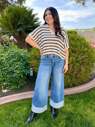 A woman wearing high-waisted cuffed wide-leg jeans in a medium wash and black boots.
