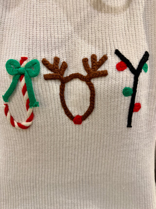 Close-up of a sweater with Christmas-themed appliqués including a candy cane, reindeer antlers, and a tree.