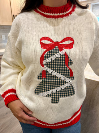 White sweater with a Christmas tree design and red trim worn by a person.