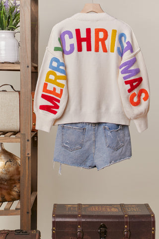 Beige sweater with colorful 'Merry Christmas' text on a neutral background
