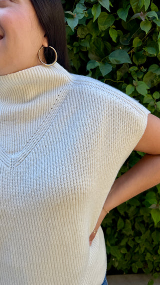 Woman wearing a ivory knitted sweater vest and blue jeans.
