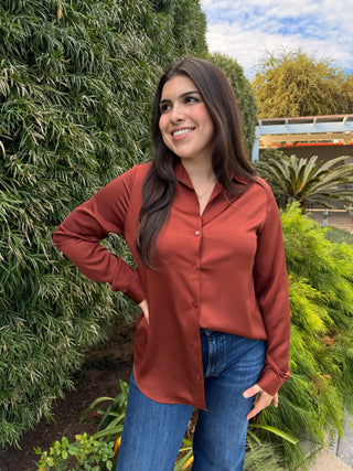 A woman wearing a brown long sleeve button-down shirt and blue jeans.