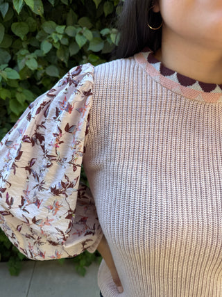 A woman wearing a pink knitted sweater with a floral print on the sleeves. 