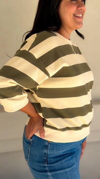Side view of a women's olive and cream bold stripe top showing the relaxed fit and ribbed hem