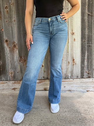 Woman wearing light blue jeans standing against a wooden fence.