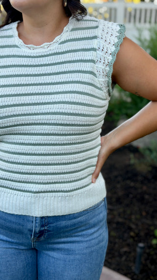 Woman wearing a white and sage striped sleeveless crocheted knit top.