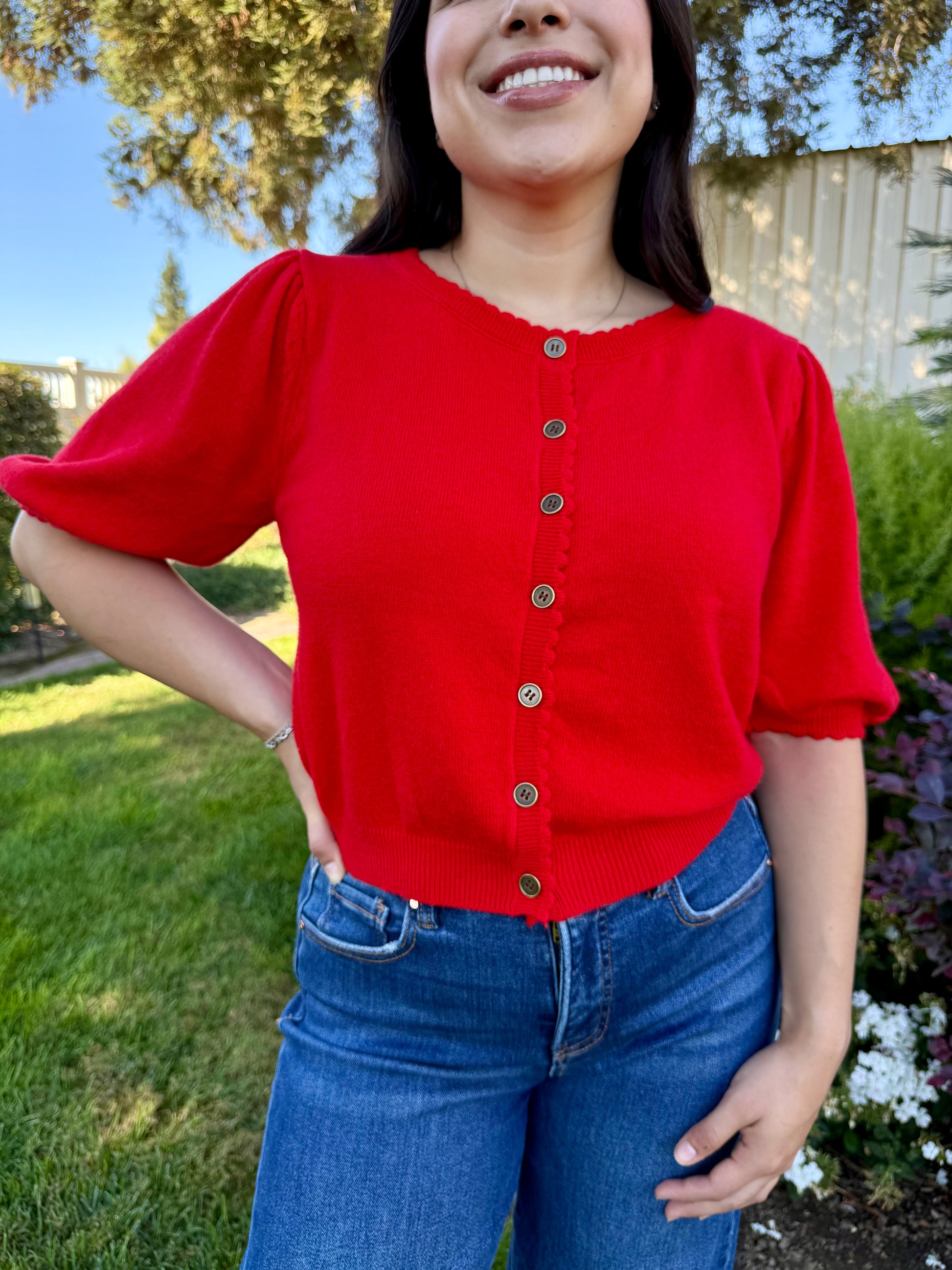 Person wearing a red cardigan with short sleeves and blue jeans outdoors.