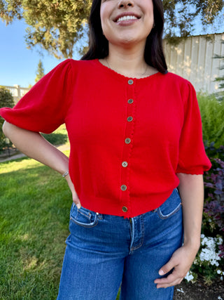 Person wearing a red cardigan with short sleeves and blue jeans outdoors.