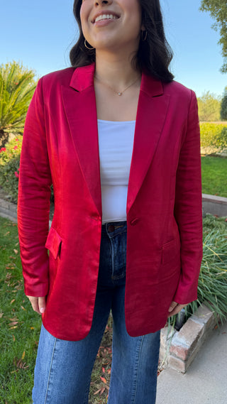 Woman wearing a long sleeve red satin blazer and blue jeans.