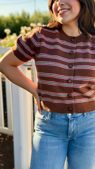 A woman wearing a brown sweater with pink and teal stripes. 