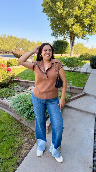 Woman wearing a brown sleeveless sweater with decorative black and white trim.