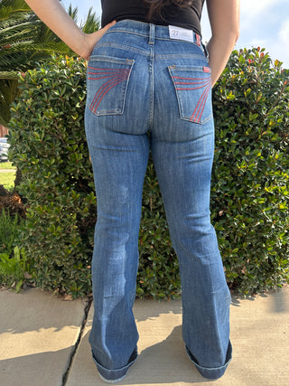 A woman wearing dark blue jeans with a red 7 stitched on the back pocket. 