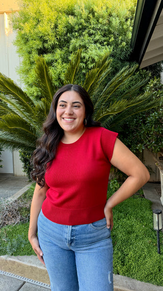 Woman wearing a cherry red cap sleeve knit sweater top with a ribbed hem.