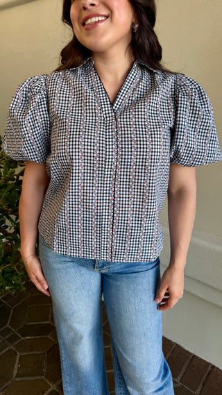 A woman wearing a black plaid blouse with jeans.