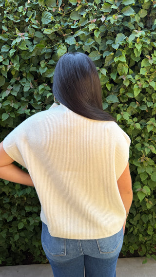 Woman wearing a ivory knitted sweater vest and blue jeans.