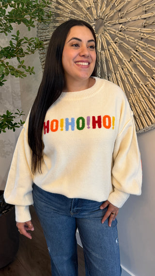 Woman wearing a cream sweater with 'HOHOHO' in colorful letters, standing indoors.