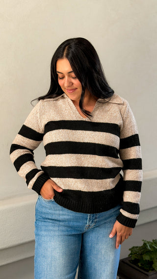 Woman wearing a black and cream striped collared V-neck sweater with light-wash jeans