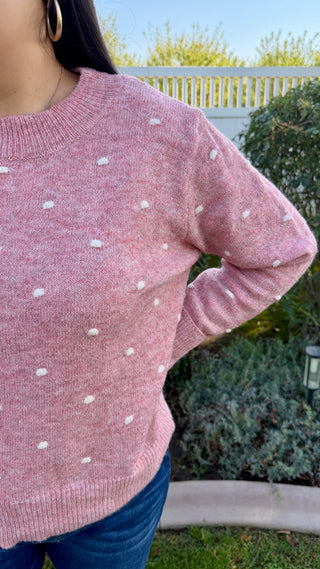 A woman wearing a pink polka dot sweater with blue jeans outdoors