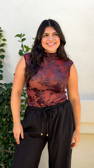 Model wearing burgundy floral sleeveless mock neck top with black wide leg drawstring pants, front view