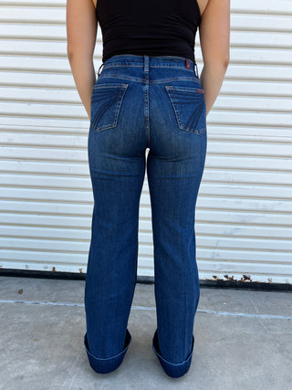 A woman wearing high - waisted jeans with dark blue 7 stitching on the back pocket. 