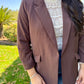 Person wearing a brown blazer over a white lace top with a blurred outdoor background