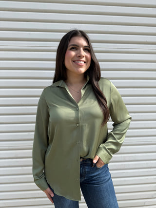 A woman wearing a green long sleeve button-down shirt and blue jeans.
