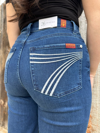 A woman wearing dark wash high waisted, wide leg jeans with a white 7 stitched on the back pocket. 