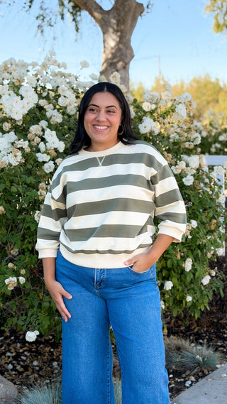 Women's olive and cream striped casual top styled with wide-leg jeans outdoors, full-length view
