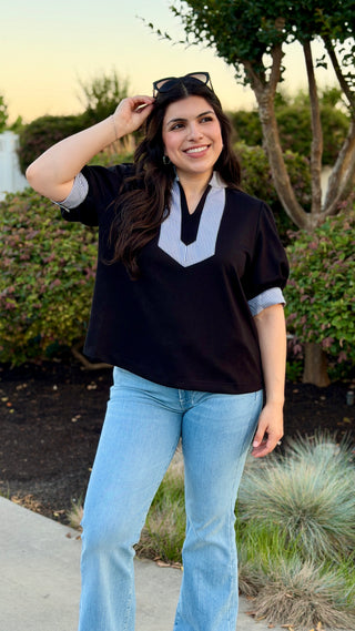 Woman wearing a black blouse with a white collar.