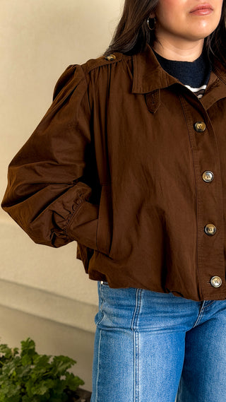 Side view of a brown cotton bomber jacket showing the gathered shoulder and button-front detail