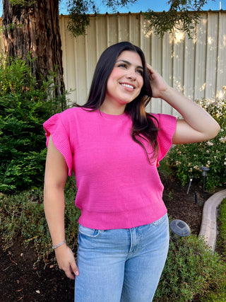 A woman wearing a pink short sleeve ruffle sweater paired with blue jeans, standing outdoors.