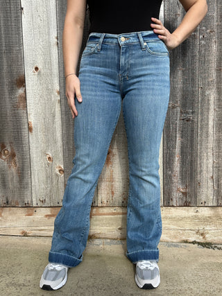 A woman wearing light wash denim trousers with a cream 7 stitched on the back pocket. 