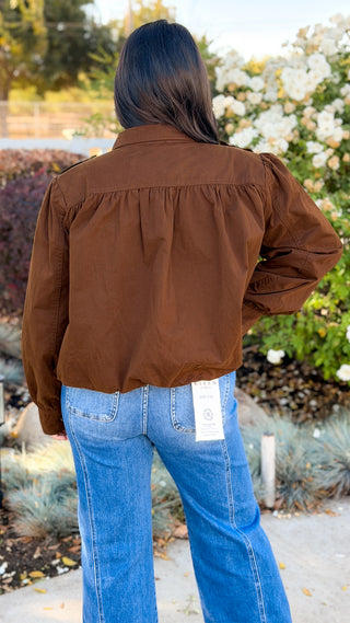 Back view of a women's brown bomber jacket showing the gathered shoulders and gathered hem