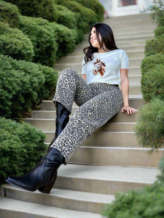A woman wearing high waisted leopard print barrel leg pants with a light colored top and cowgirl boots. 